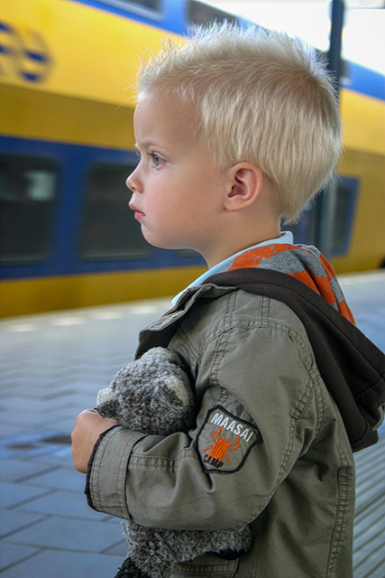 Jongetje met knuffel onder de arm staat op perron bij passerende trein