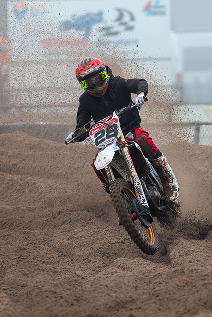 Motorcrosser op een zandcircuit met opspattend zand