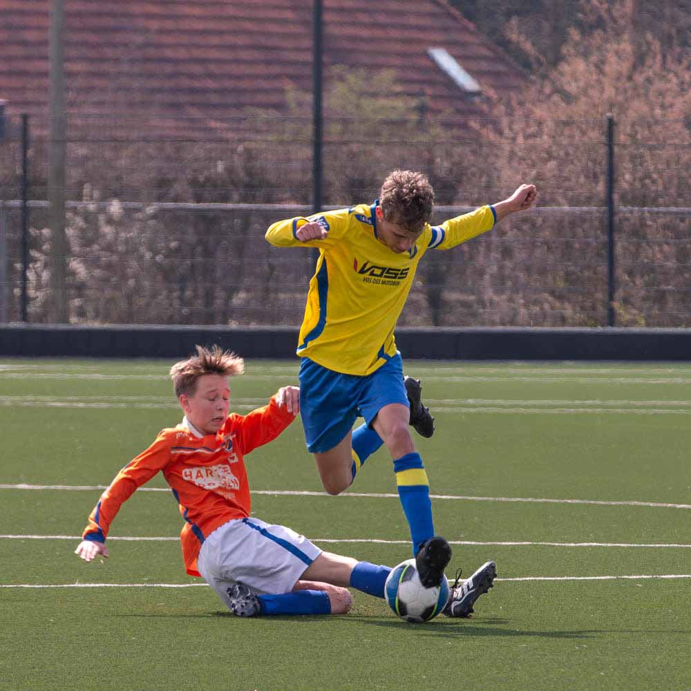 Voetbalduel, een voetballer springt over een sliding makende tegenspeler